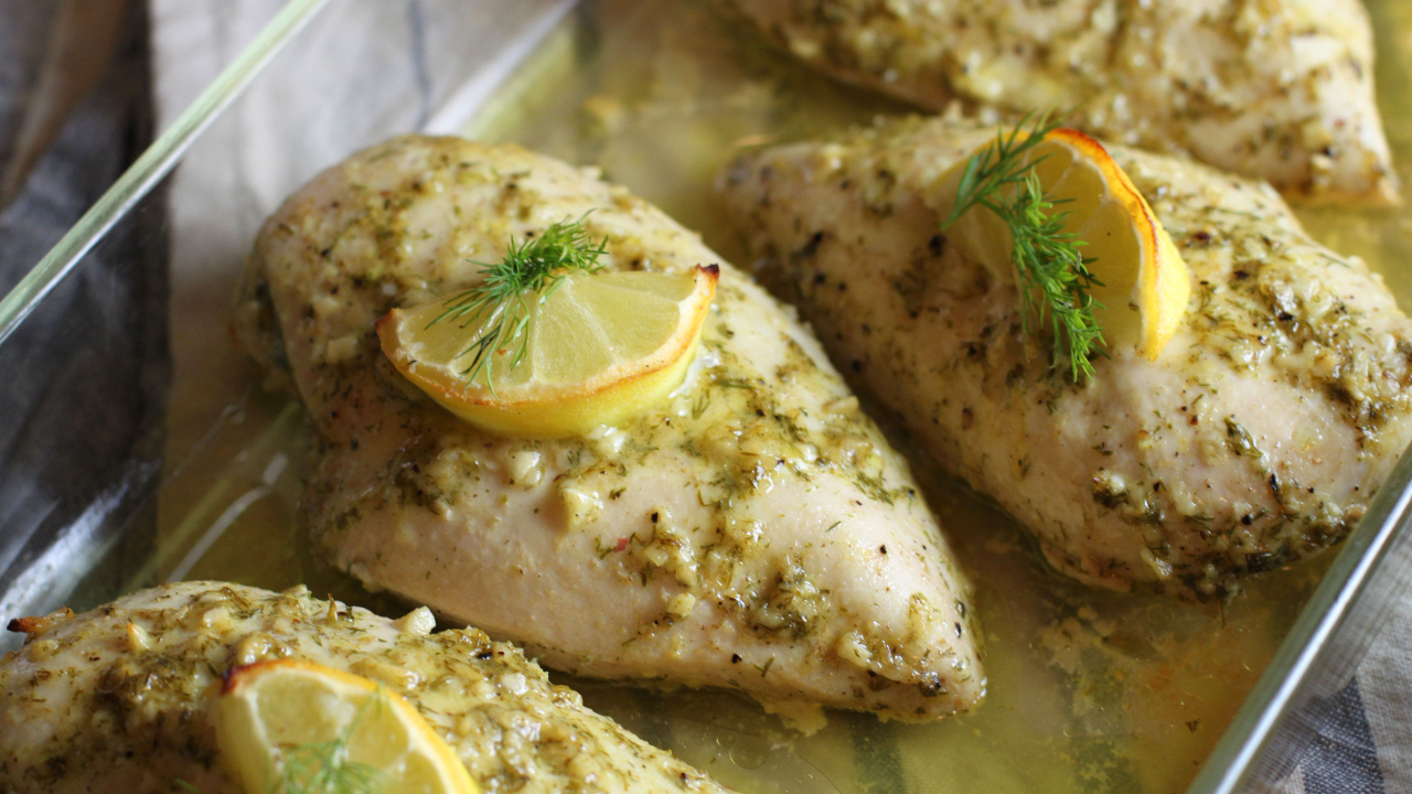 Four chicken breasts coated with a dill and garlic marinade, and topped with a slice of lemon and a sprig of fresh dill, then baked in a glass dish