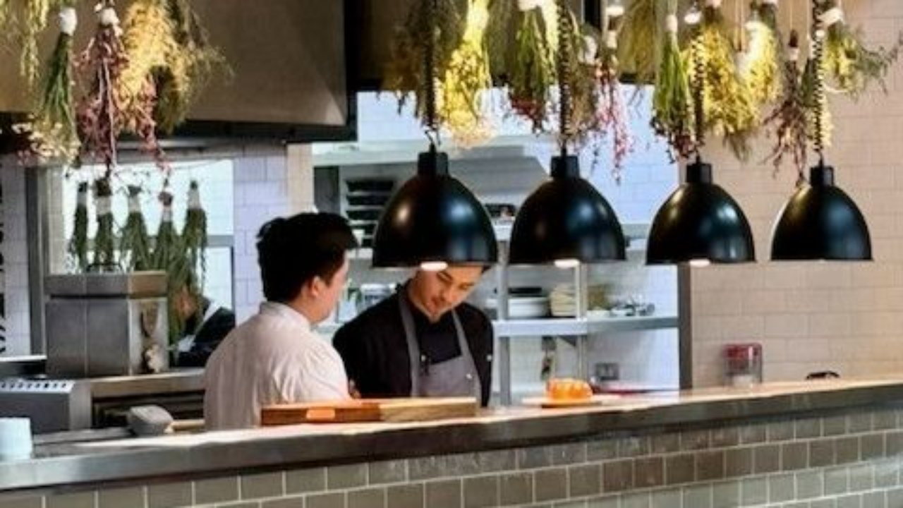 Open kitchen restaurant staff preparing food with hanging herbs and modern lighting, highlighting hospitality and customer experience