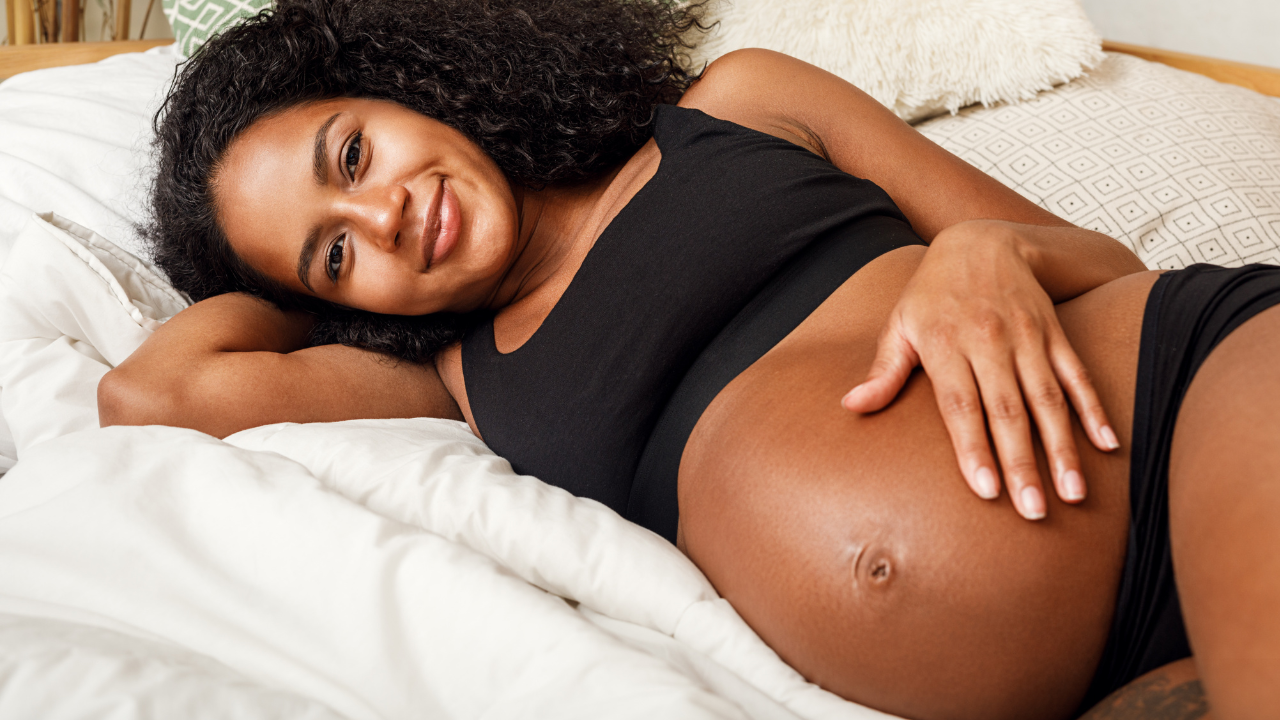 Black, smiling, pregnant woman reclines on bed at home