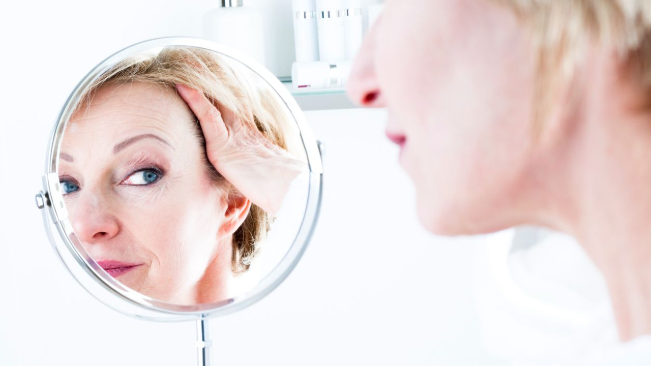 Mature woman thoughtfully examining skin concerns in vanity mirror inside her  bathroom.