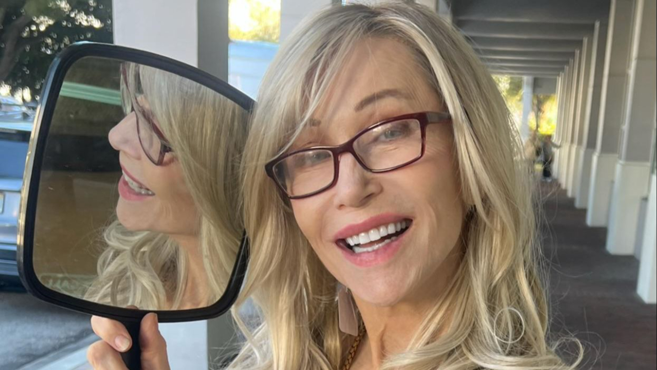Woman holding a mirror showing her reflection, smiling with long blonde hair, representing confidence and healthy aging.
