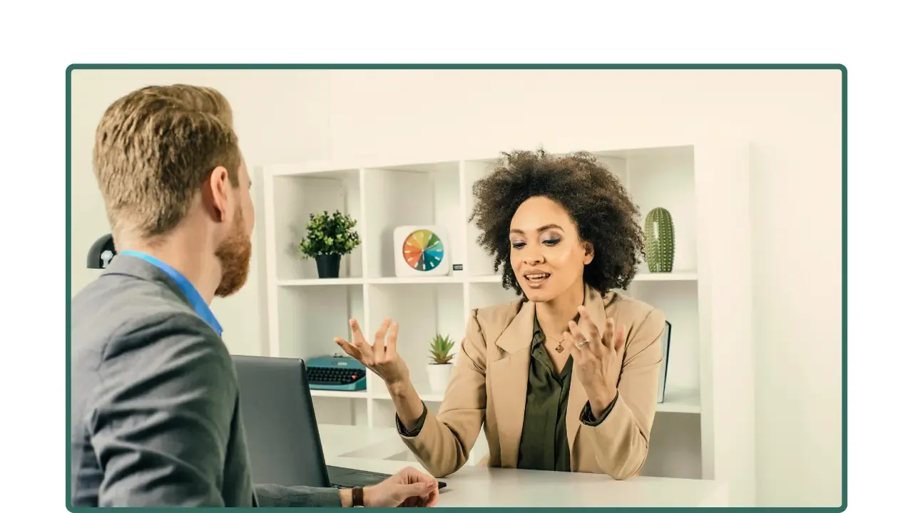 Dos personas conversan frente a frente en una oficina, mostrando una conversación atenta más allá de solo dar indicaciones.