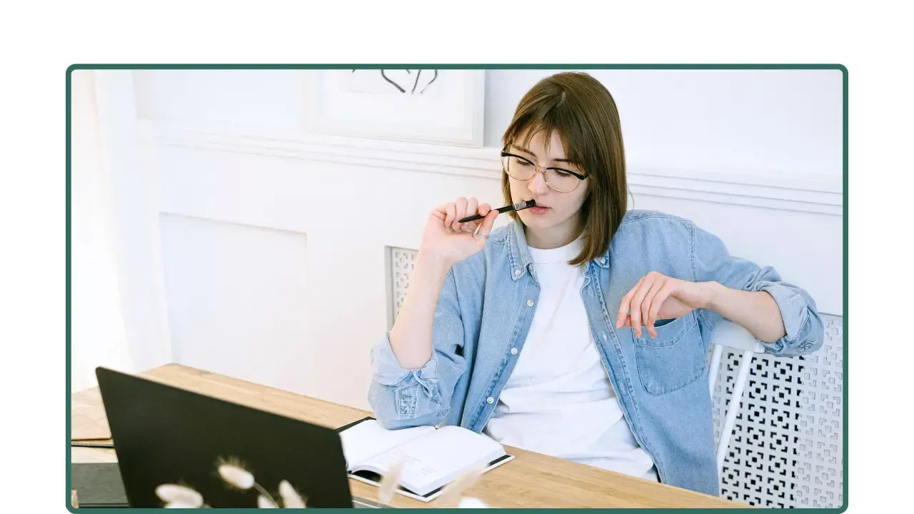 Mujer trabajando en su escritorio con portátil y cuaderno, en un momento de reflexión