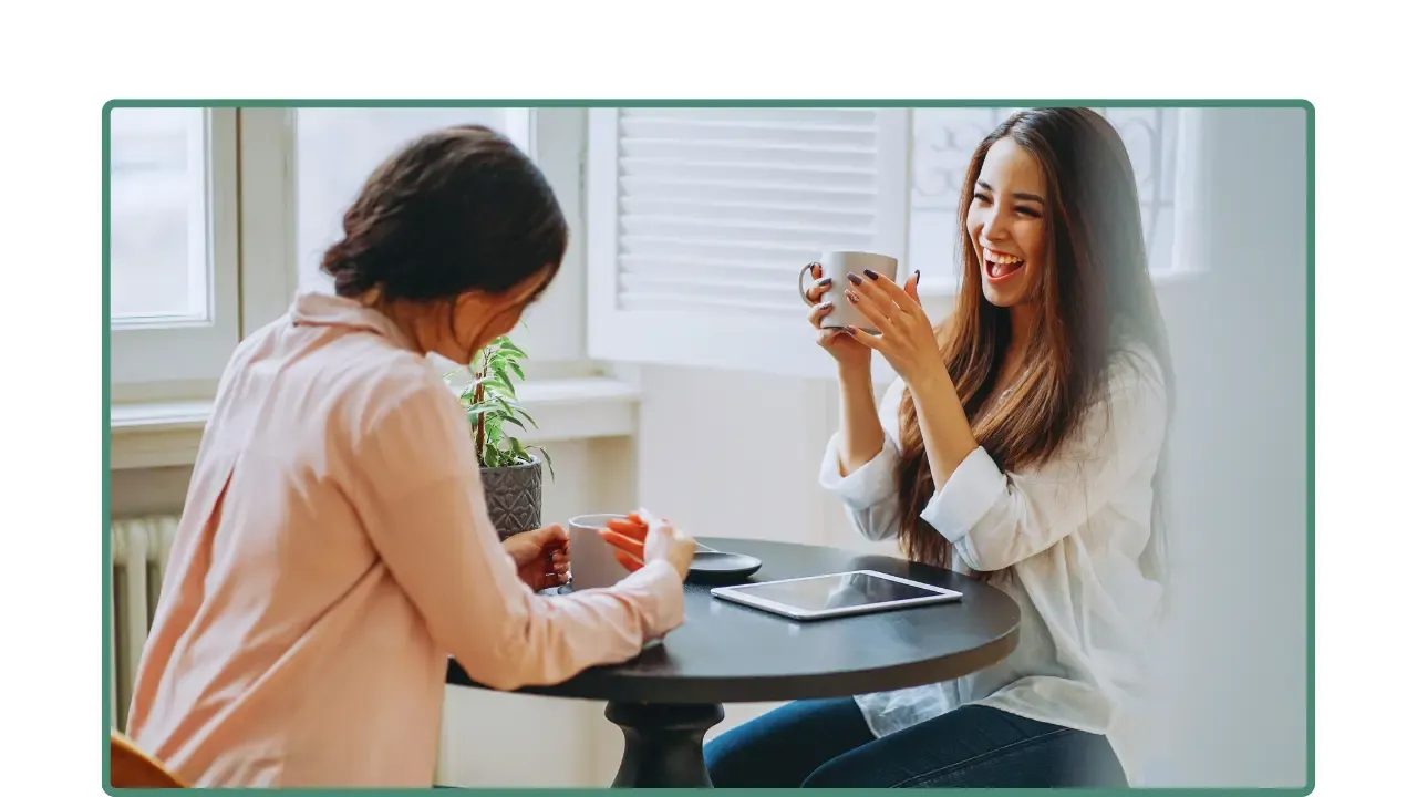 Dos mujeres conversando con confianza en una mesa pequeña, en un ambiente luminoso.