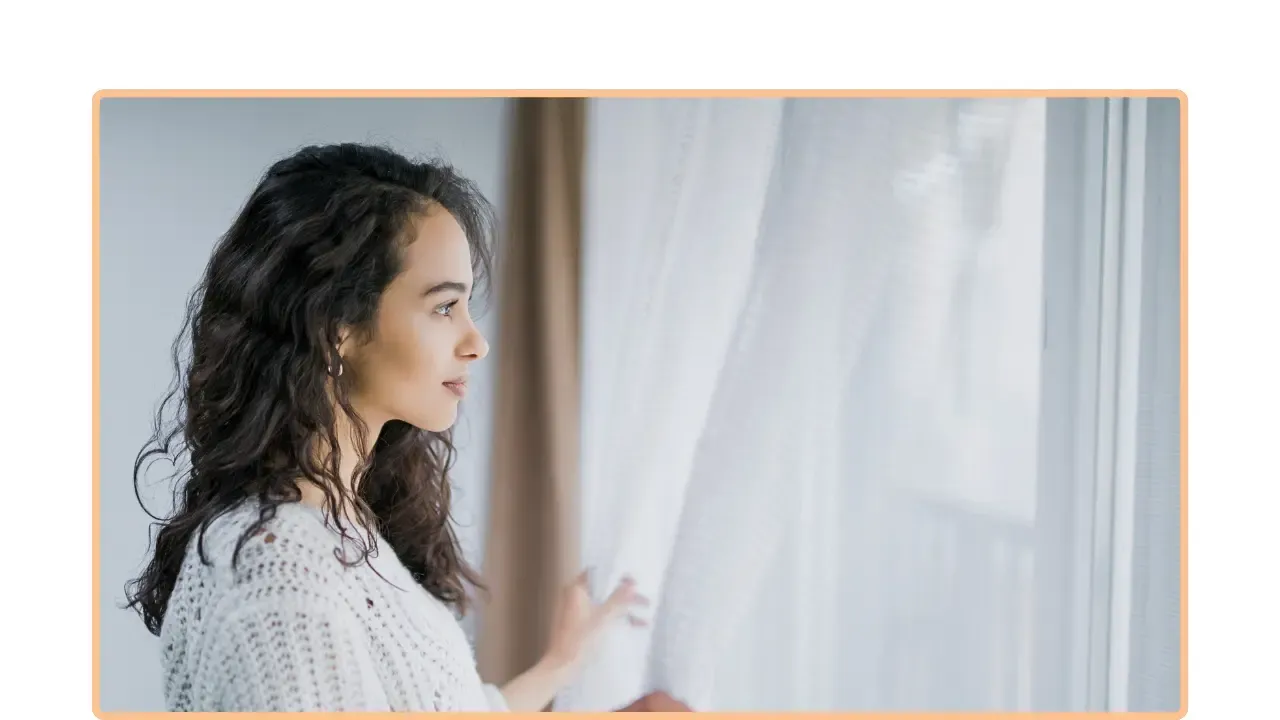 Persona de perfil junto a una ventana con cortinas blancas, mirando hacia la luz natural, en un nuevo comienzo