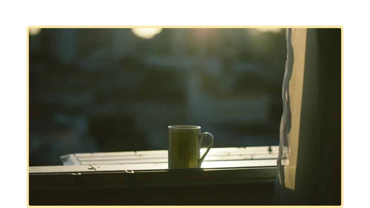 Una taza en el borde de una ventana con luz suave y la ciudad desenfocada al fondo.