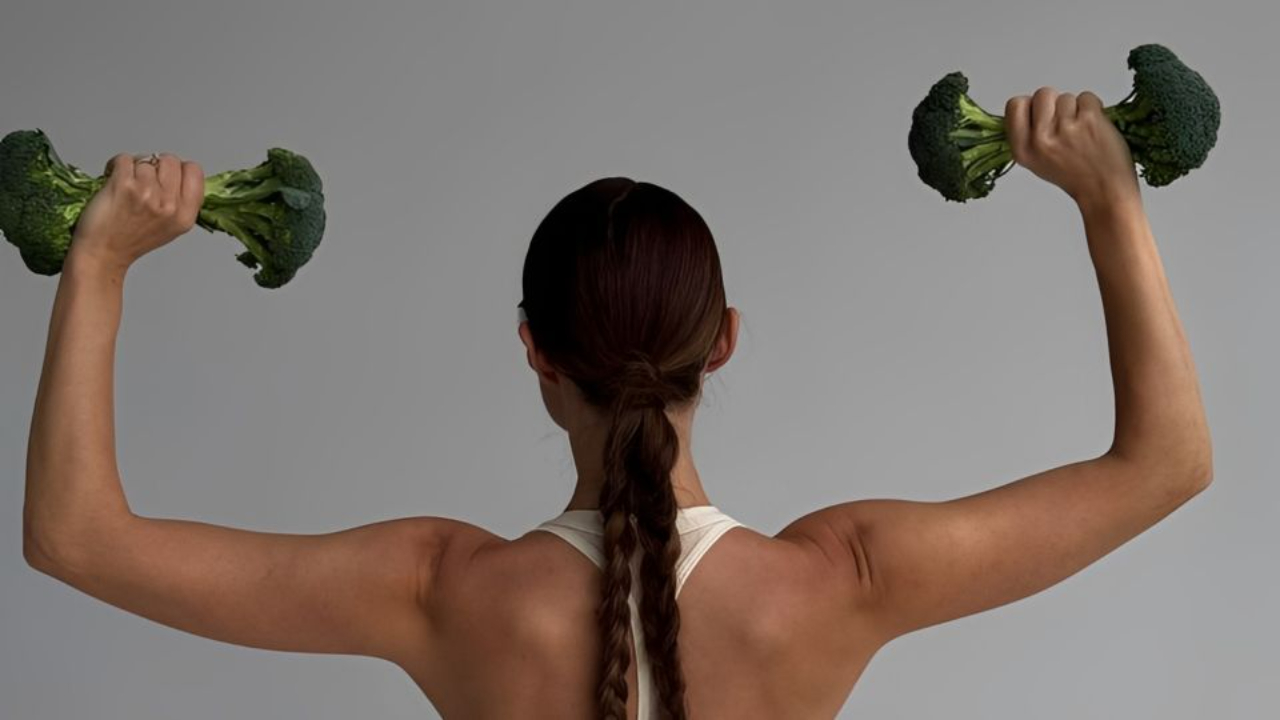 Fitness-focused woman lifting broccoli as weights, highlighting strength training, muscle building, and balanced nutrition for women’s health in 2026