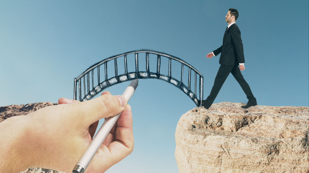 Businessman walking while a giant hand draws a bridge to fill the gap between cliffs