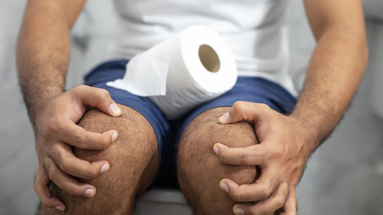 man sitting on toilet straining due to constipation