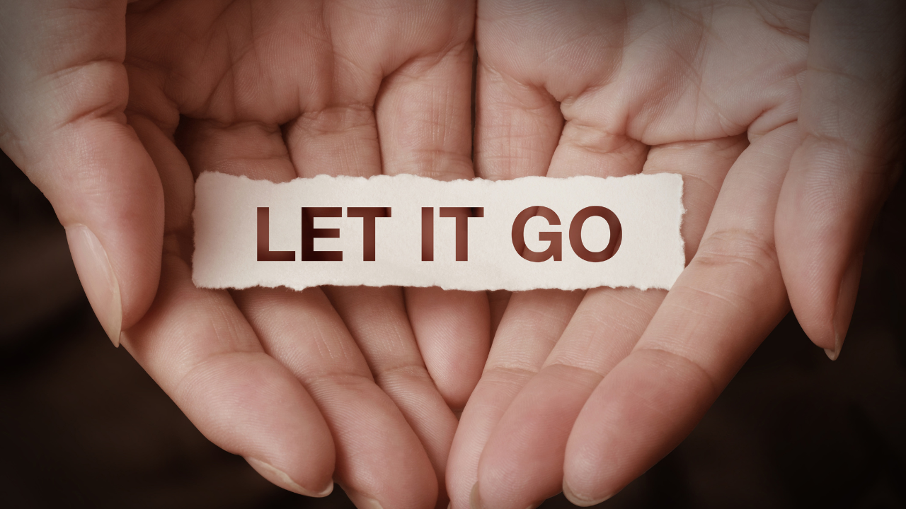 Hands gently holding a torn piece of paper that says let it go.