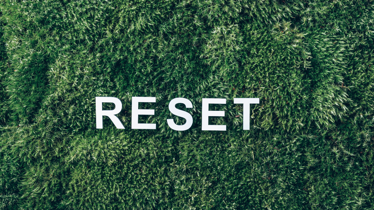 the word reset spelled in white letters against a textured green grass background, symbolizing a calm and grounded fresh start