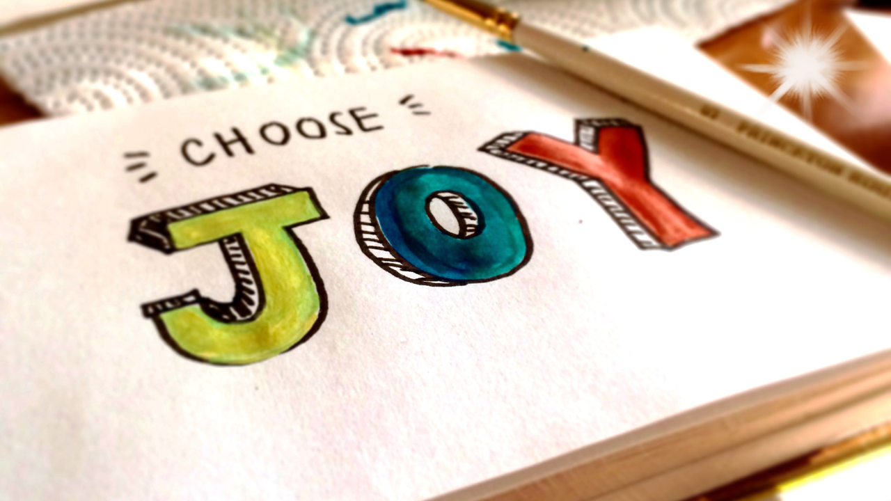 close-up of a hand-painted page with the colorful words “Choose Joy,” symbolizing positivity and emotional well-being