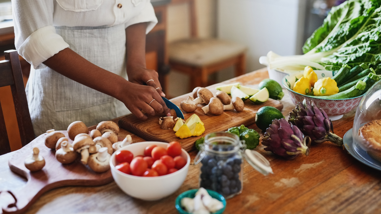 woman preparing fresh vegetables and whole foods in a kitchen, symbolizing simple, realistic nourishment that supports energy, hormones, and everyday life without restriction