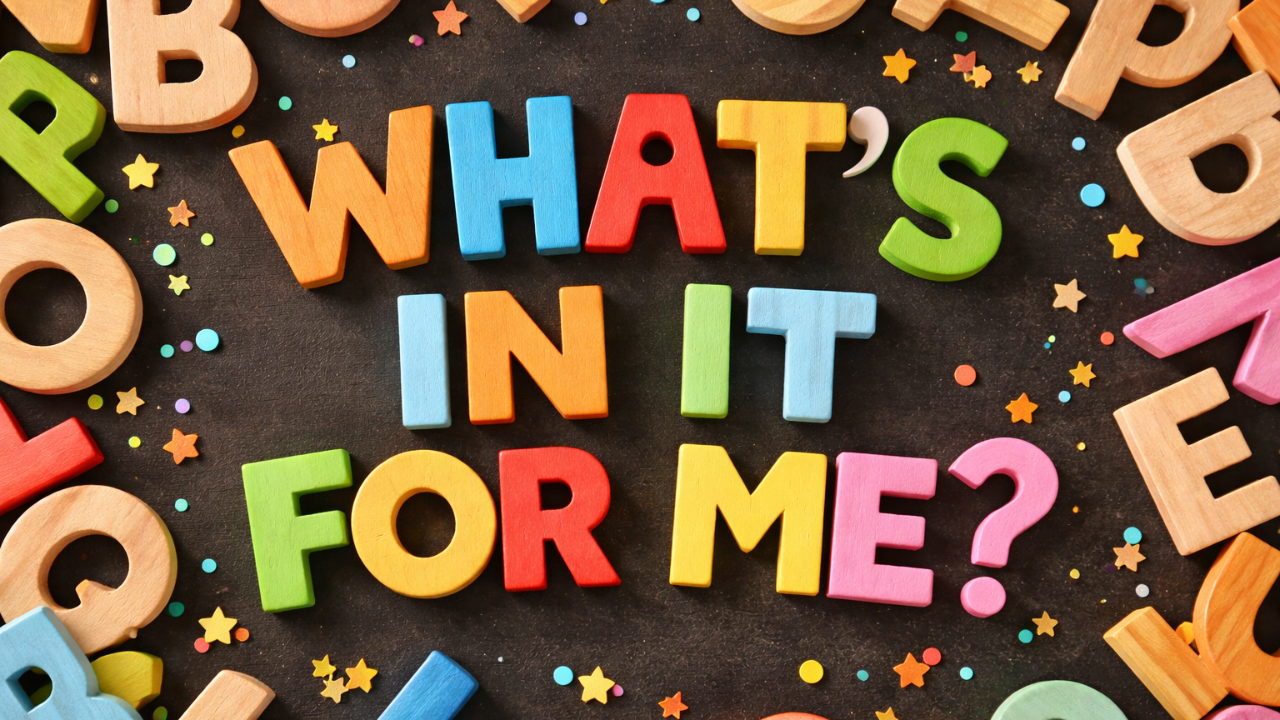 Colorful wooden alphabet blocks arranged to spell “What’s In It For Me?” on a dark background, with scattered bright letters and playful decorative accents surrounding the phrase.