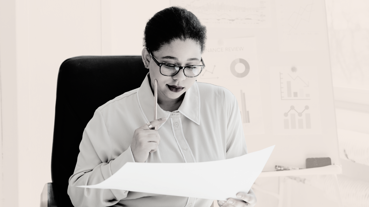 Black woman in glasses reading financial documents at her desk, representing emotional intelligence, reflection, and resilience in women-led business leadership.