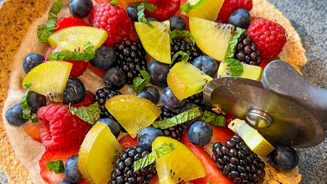 Fruit pizza with berries being cut with a pizza cutter.