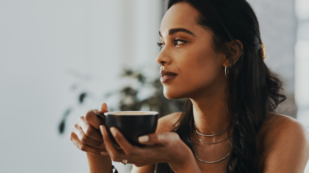 Woman gently looking forward holding a coffee cup. She has long brown hair.