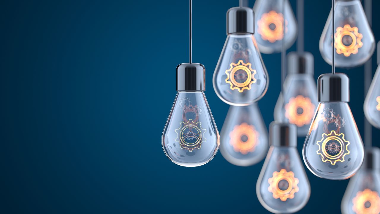 several clear light bulbs with gears inside hanging down on poles