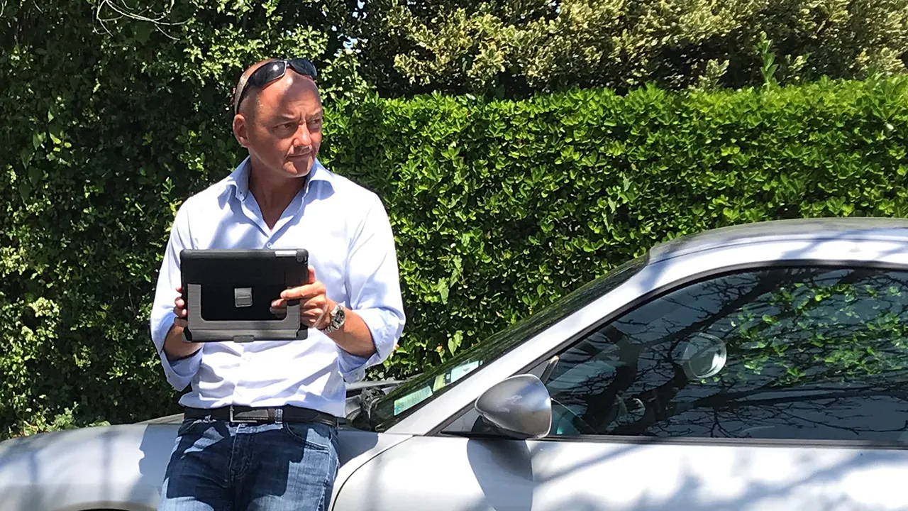 Andy Brown - Kajabi Expert standing next to a car, holding an iPad