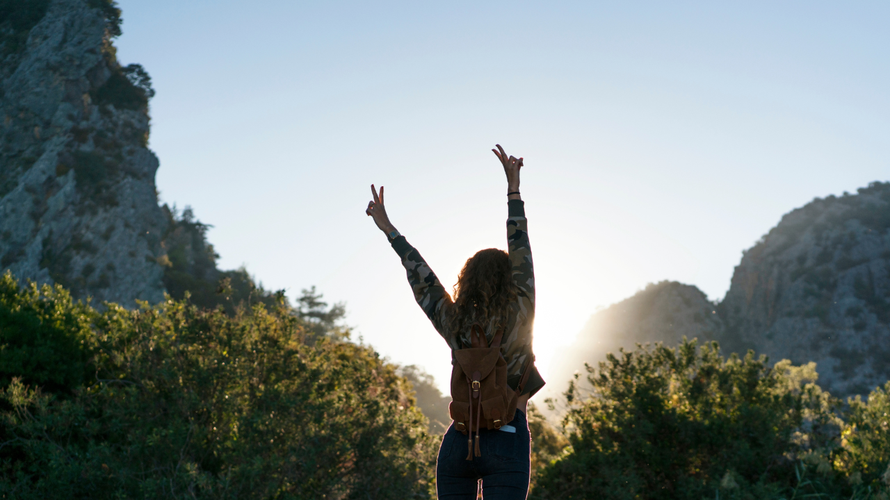 Vrouw die haar armen omhoog heft in de bergen, als symbool voor het voelen van haar interne grens en leven vanuit haar waarheid – systemisch werk en coaching.