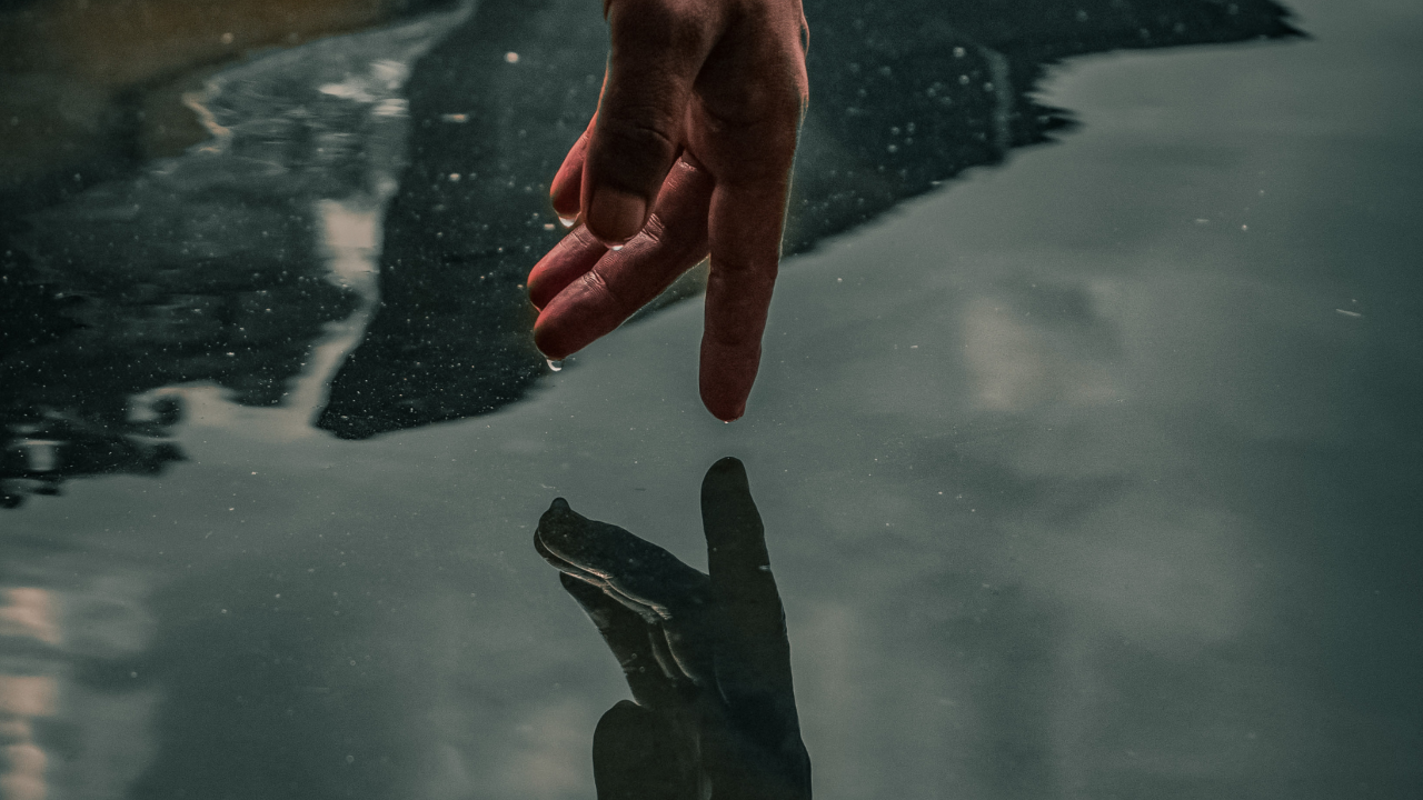 Twee handen die elkaar raken op een bevroren ijsoppervlak, symbool voor afstand, breuk en verlangen.