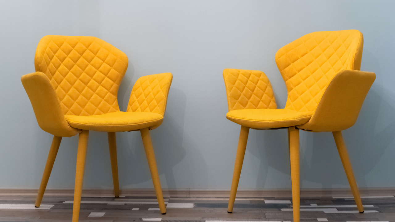 Twee gele stoelen tegenover elkaar, als symbool voor een veilig en open gesprek in coaching.