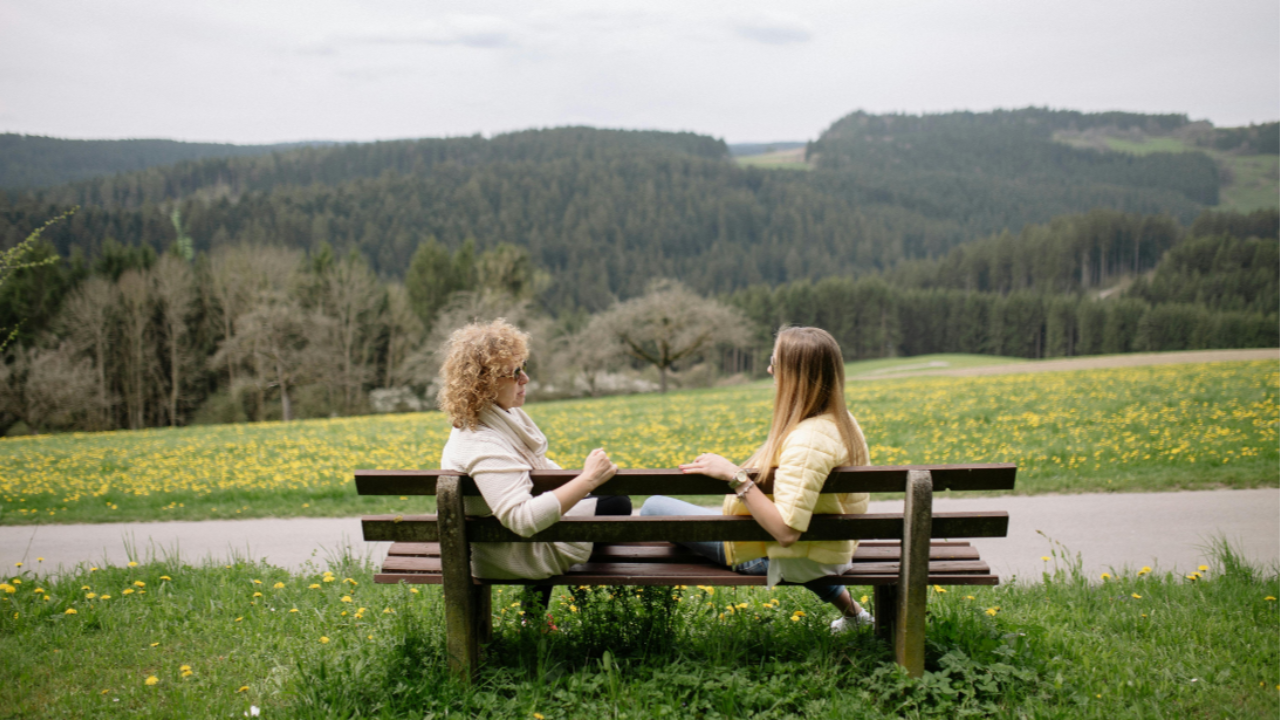 Two women sitting on a bench in nature having a heartfelt conversation, supporting each other