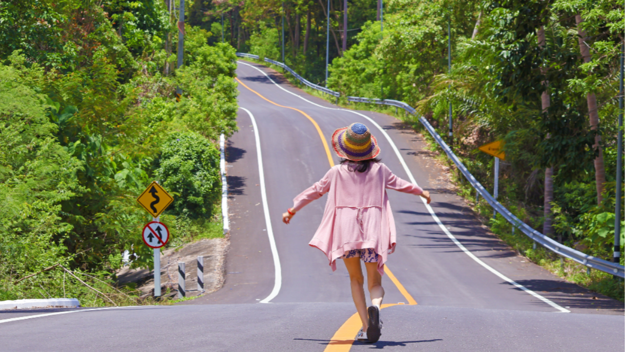 Woman running freely along a winding coastal road symbolising freedom, presence, and letting go of expectations