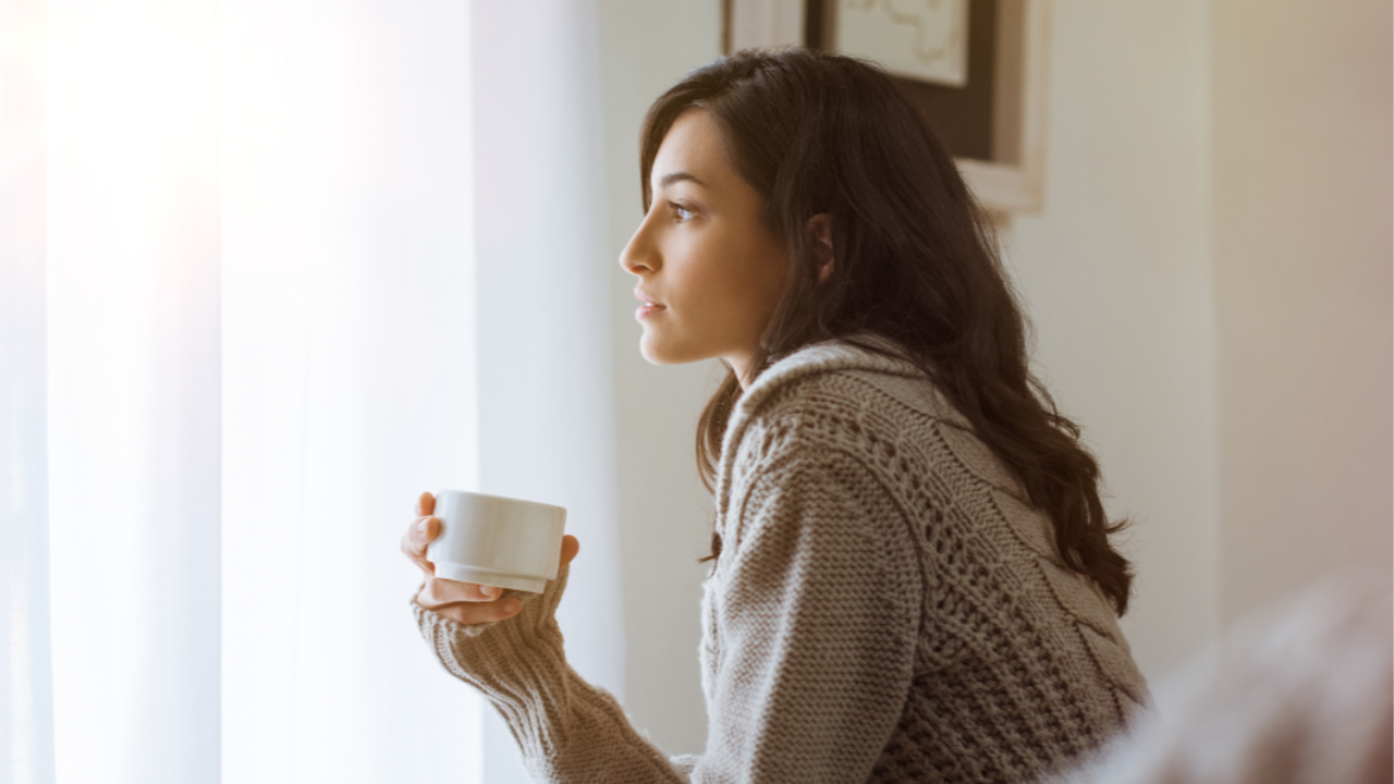 Woman sitting by a window with a cup of tea, reflecting during an emotionally overwhelming day