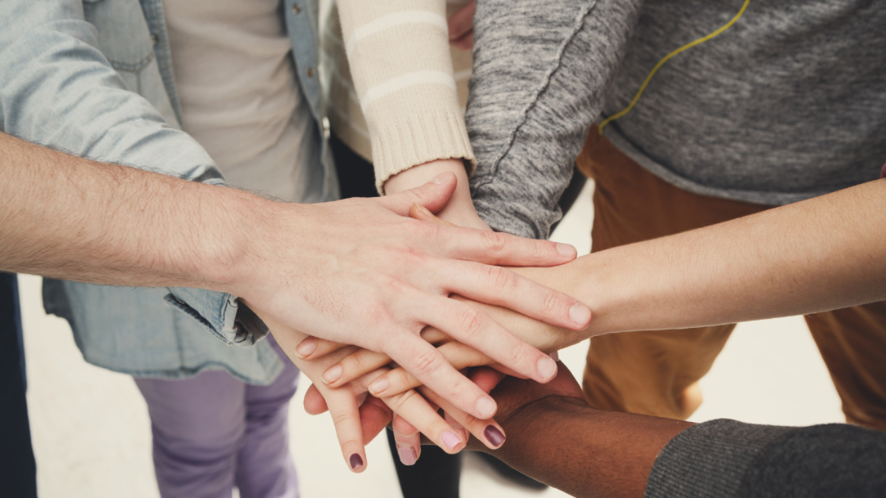 A group of people placing their hands on top of each other in a gesture of unity, trust, and connection