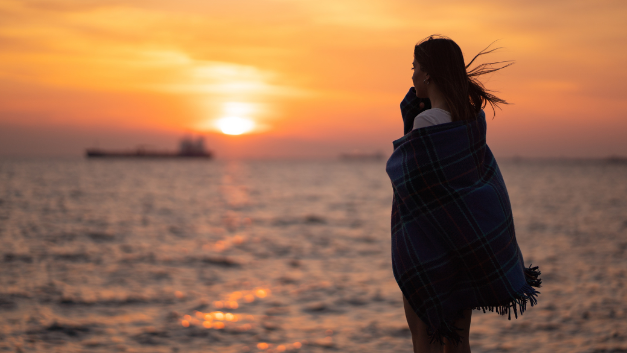 Woman looking out to sea at sunset reflecting on life and feeling overwhelmed while building a business