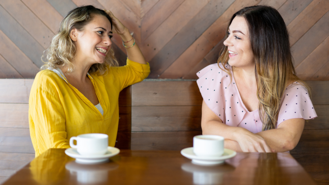 Two women smiling and chatting over coffee, enjoying each other's company
