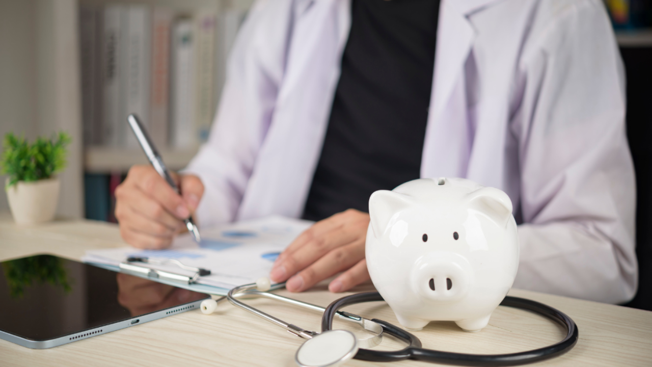 Doctor with stethoscope and white piggy bank on desk symbolising financial health, saving money, and building long term wealth