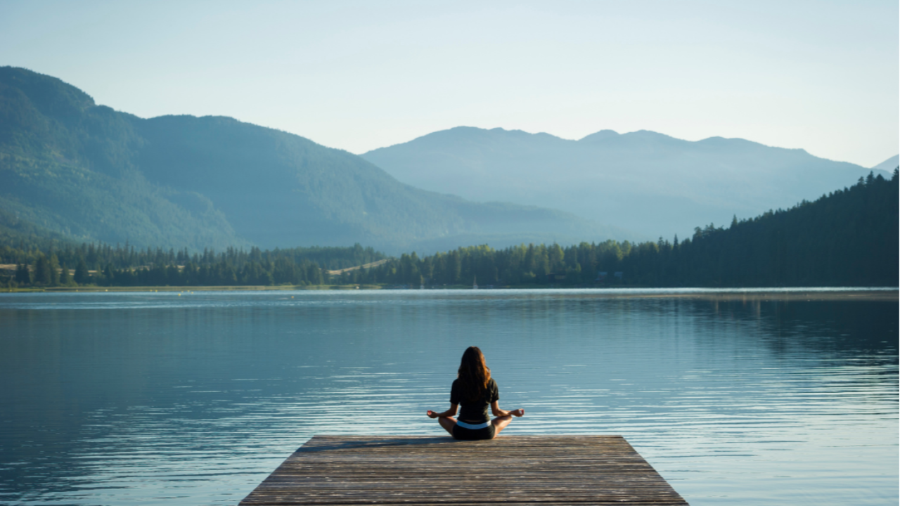 Woman meditating by a serene lake in nature, connecting with her inner peace