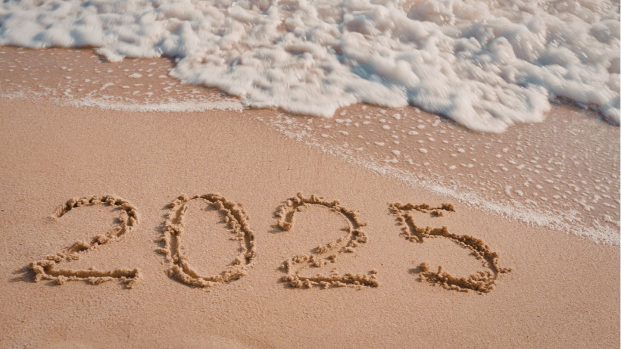 Incoming tide washing away “2025” written in beach sand
