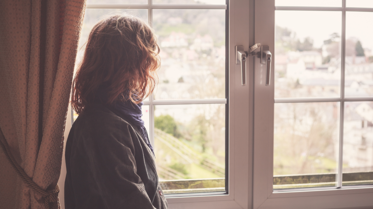 Woman looking out of a window symbolising loneliness and social isolation
