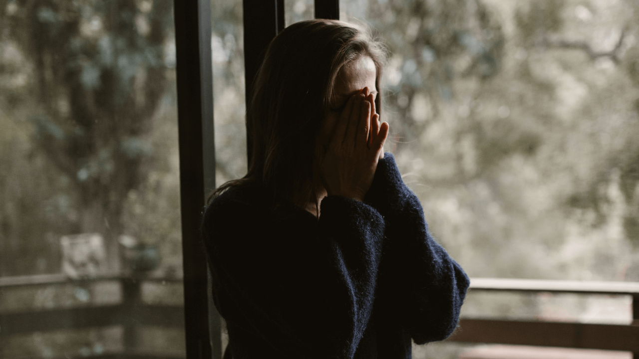 Frustrated woman with PTSD memory loss standing outside with hands up by face.