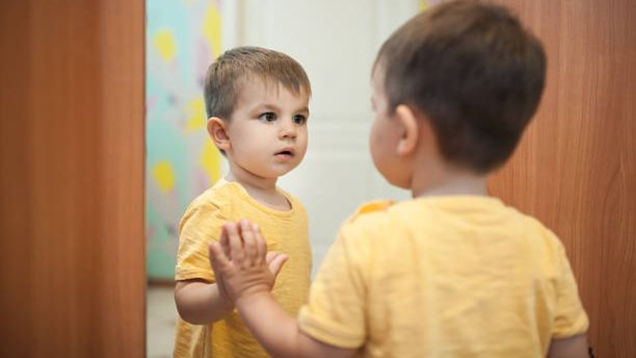 child with serious face and hand up to mirror is looking at themself.