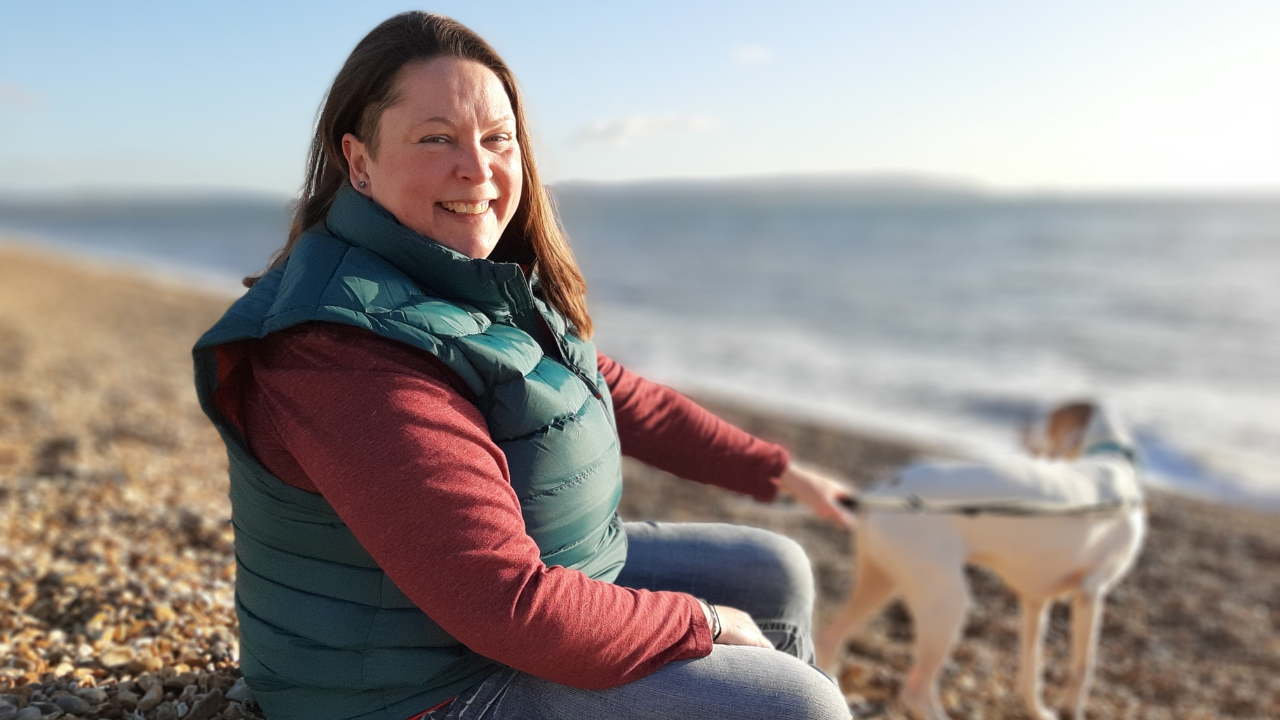 Lady sat on pebble beach with white and brown dog on lead