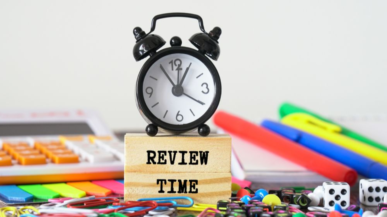 Clock sitting on a block reading "Review Time" surrounded by office supplies