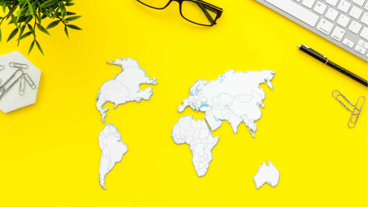 A yellow desk with pictires of the American and African Continents and other office objects such as paper clips, a pen, and a keyboard.