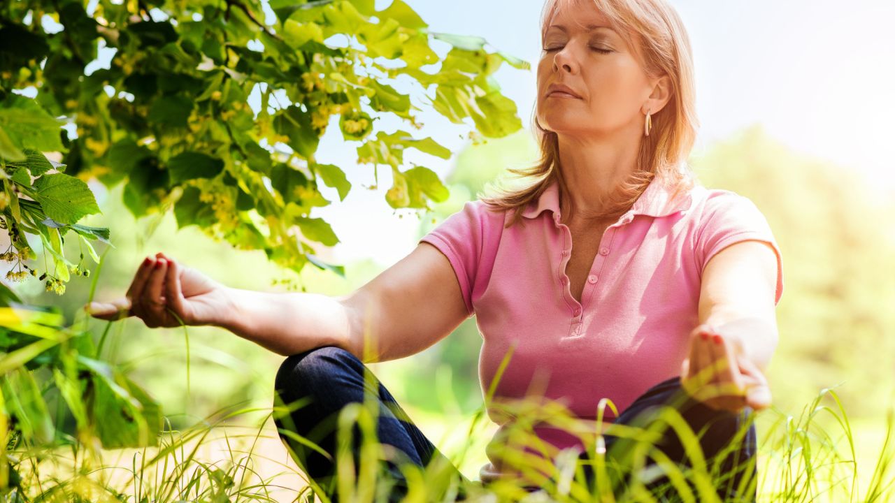 middle-aged woman meditating as she sits crosslegged in the grass