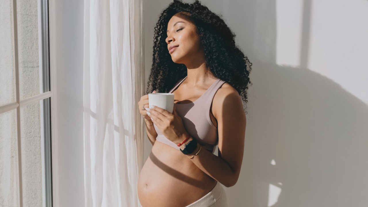 pregnant women standing in front of a window holding a cup of tea