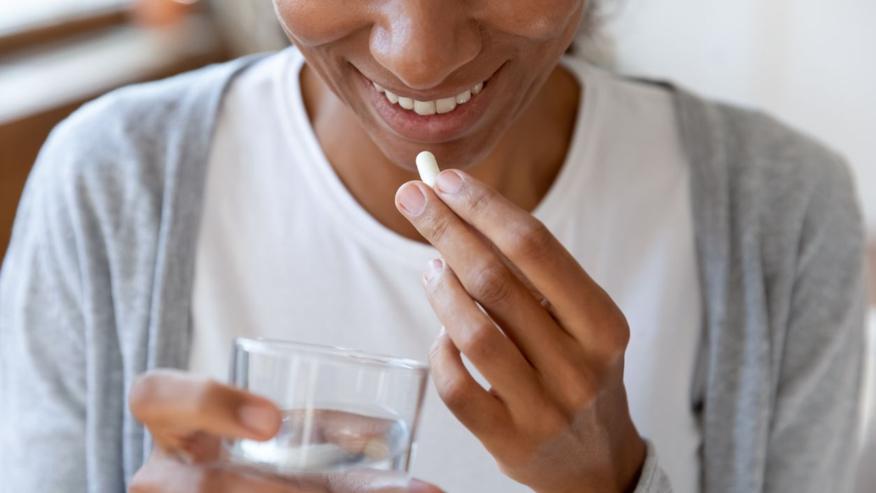 woman holding a glass of water and taking a supplement