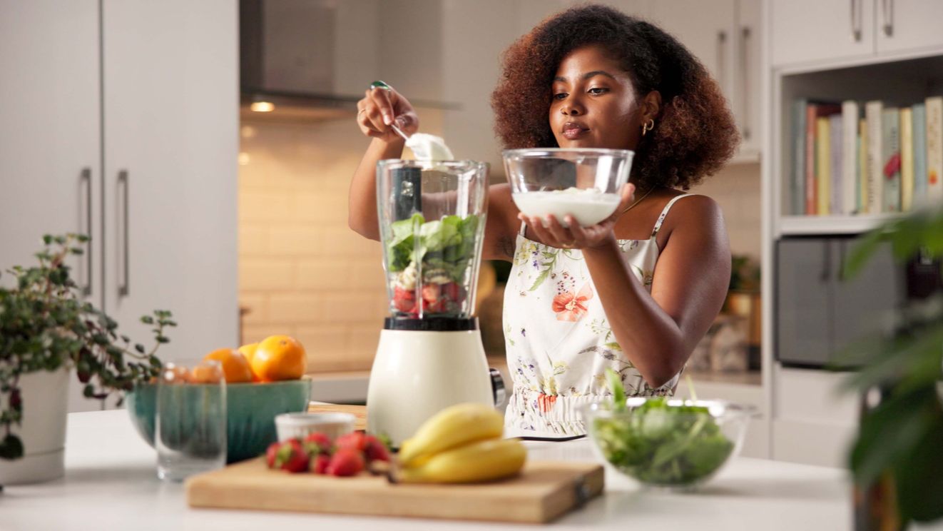 African American woman in a beautiful white kitchen making a smoothie
