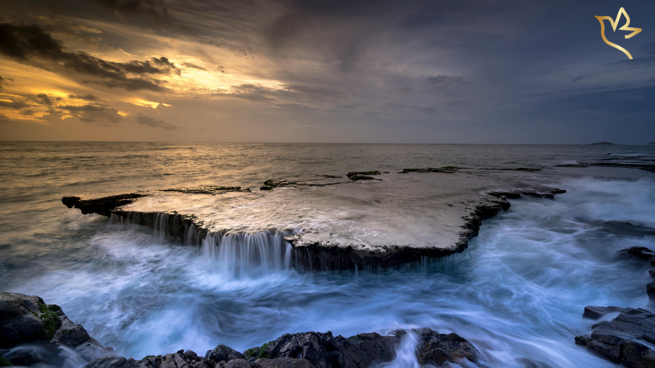 A calm ocean scene at sunset with waves gently flowing over rocks, symbolizing the quiet and emotional stillness many feel after a funeral ends.