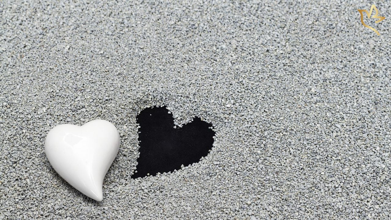 White ceramic heart resting beside a heart-shaped imprint in gray sand — symbolizing loss, remembrance, and the quiet peace found in simplicity.