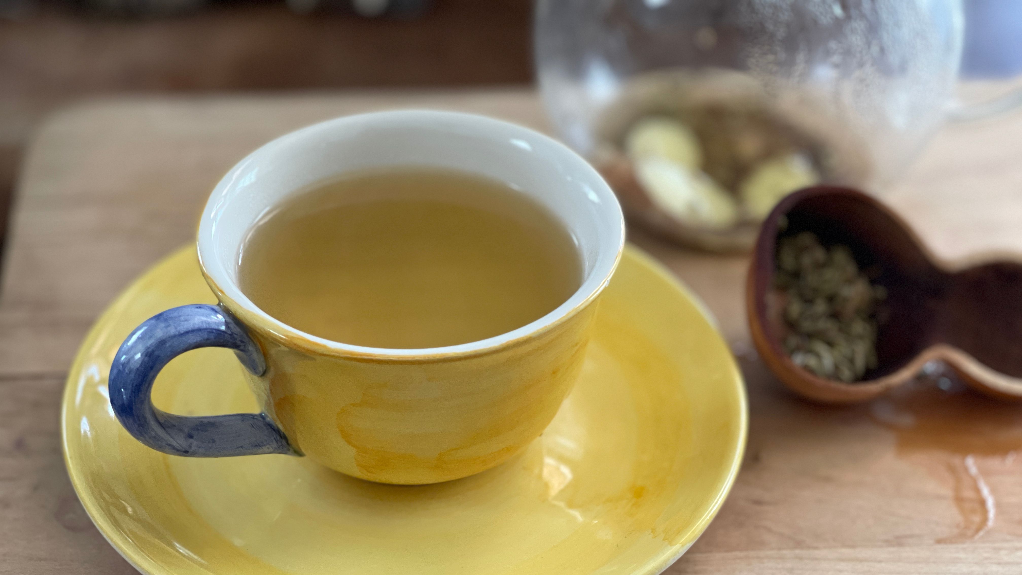 yellow cup of tea with gourd and mason jar of ingredients in back