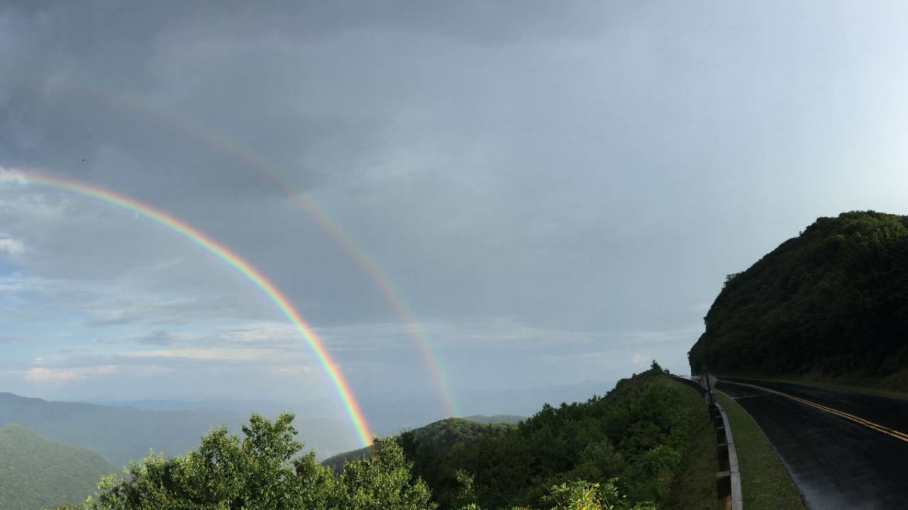 Rainy road with a double-rainbow in the distance.