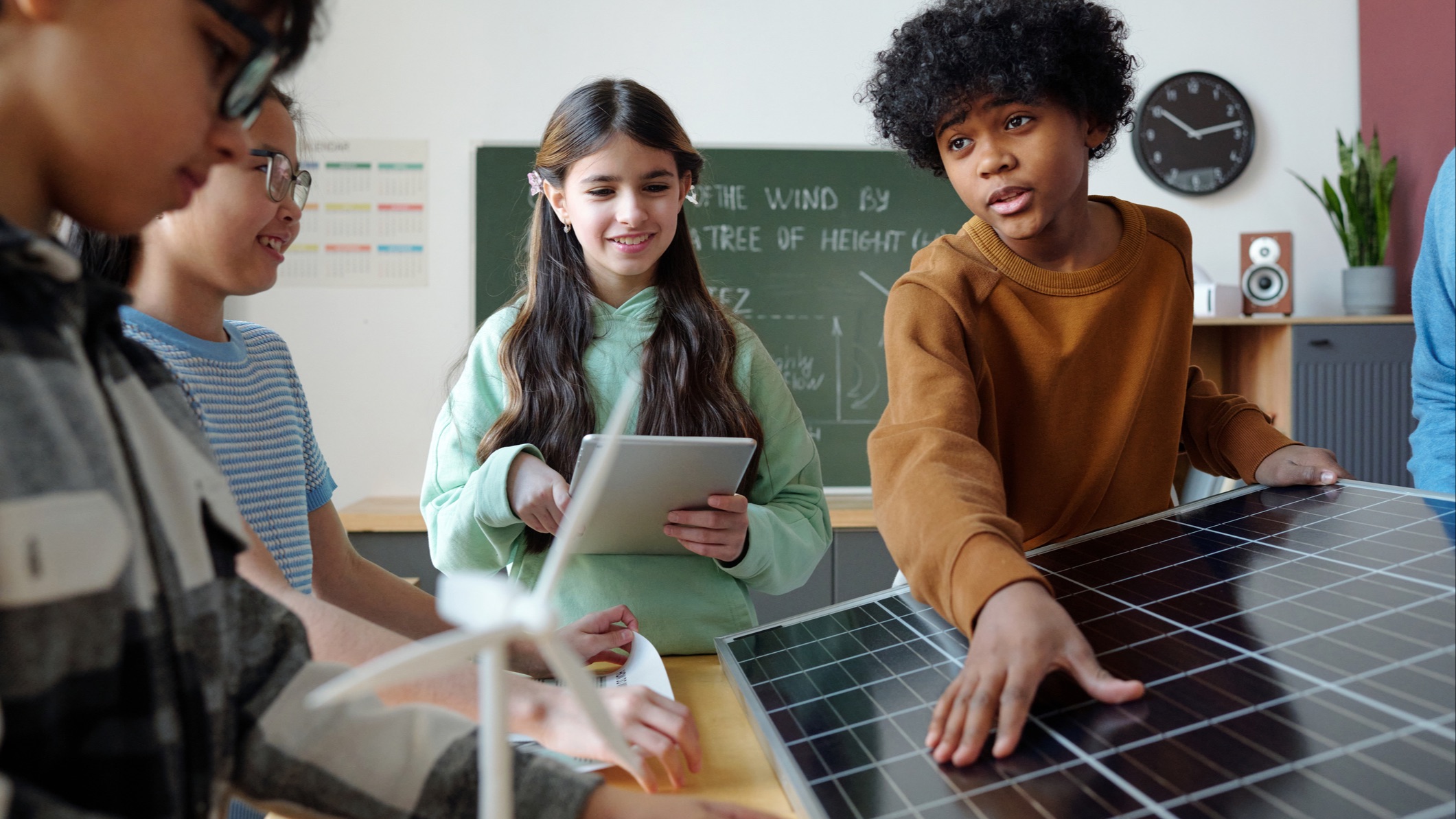 4 children in class, wind turbine and solar panel on desk
